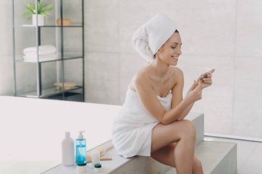 Kız pakette kozmetik malzemeleri listesini okuyor ve gülümsüyor. Banyo yaptıktan sonra havluya sarılmış muhteşem Avrupalı kadın. Kaplıca merkezindeki genç bayan. Doğal kozmetik ve sağlık kavramı.