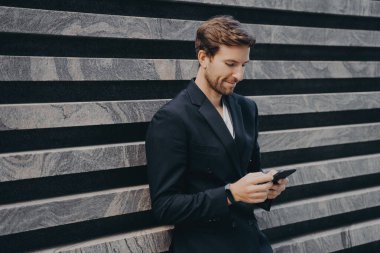 Resmi şık takım elbiseli dalgın bir ofis çalışanı elinde cep telefonu, son e-postaları ya da mesajları okuyor, önemli yazışmalara cevap yazmaya çalışıyor.