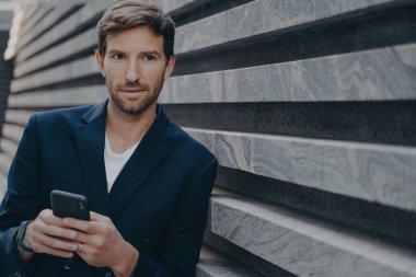 İşadamı mesafeyi düşünceli bir şekilde inceliyor. Akıllı telefon kullanıyor. Kariyeri hakkında düşünüyor. Modern aletle çalışan bir erkek.