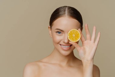 Güzel görünümlü esmer kadın portresi doğal kozmetik kapak örtüsünü seçiyor taze sulu limon tebessümleri ile diş macunuyla organik güzellik ürünleri sunuyor iç mekanda üstsüz poz veriyor..