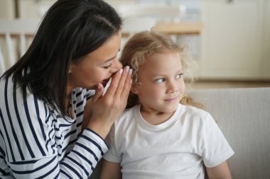 Genç anne küçük kızına bir sır fısıldıyor. Sevgi dolu bir ailenin mutlu anları olur. Genç Avrupalı anne ve çocuk evdeki oturma odasında. Bağlanma ve birliktelik kavramı.