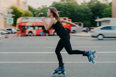Yaz boyunca tekerlekli patenlerle paten süren genç ve fit bir kadın yoğun bir yolda aktif bir yaşam tarzına sahip siyah spor ayakkabıları giyiyor ve temiz hava soluyor. Hareket kavramı.