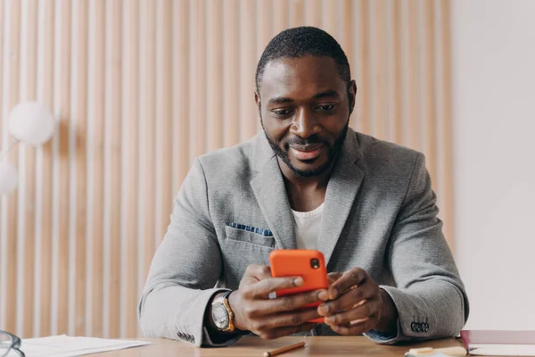 Молодой Улыбающийся Африканский Предприниматель Сидящий Рабочим Столом Пользующийся Мобильным Телефоном — стоковое фото