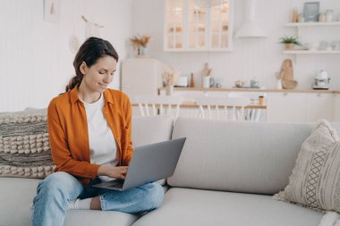 Dizüstü bilgisayar kullanan, e-posta yazan, rahat bir koltukta oturan, internetten alışveriş yapan, sosyal ağlarda sohbet eden genç bir kadın. Evde bilgisayar projesi üzerinde çalışan serbest çalışan bir kadın..