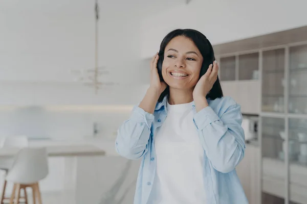 Smiling young woman listening to musical playlist in wireless headphones, enjoying music sound. Happy female listens to podcast, audio book or positive audio affirmations, resting at home.