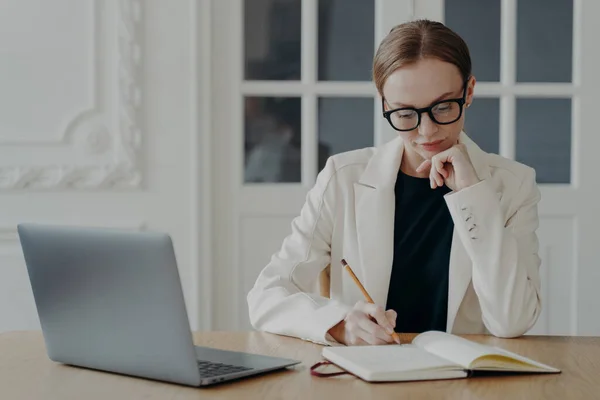 Empresária Focada Óculos Escrevendo Notebook Sentada Mesa Escritório Com Laptop — Fotografia de Stock
