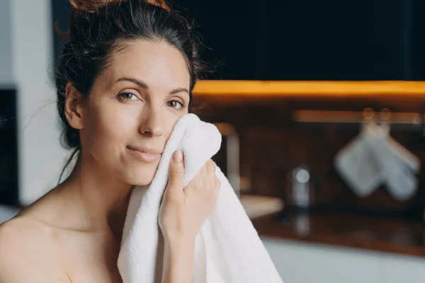 Pretty young latina woman wipe rub face with towel after shower, female do morning beauty procedures enjoying healthy smooth skin at home looking at camera. Hygiene, skincare concept.