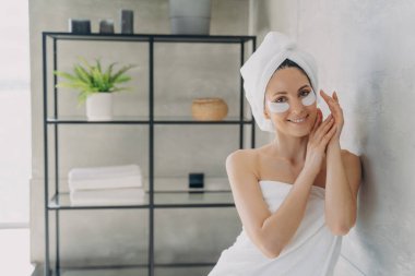 Genç mutlu kadın lüks bir spa merkezinde dinleniyor. Kız kırışıklık önleyici göz bantları yapıştırıyor. Evde sabah güzellik rutini. Banyo yaptıktan sonra havluya sarılmış çekici Avrupalı kadın.