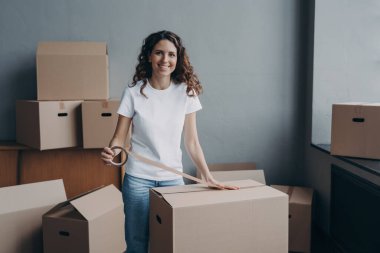 Mutlu genç bayan koli bandıyla kutuları paketliyor. Çekici bayan karton kutuları koli bandıyla paketliyor. Nakliye işçisi nakliye ve depolama için kargo hazırlıyor..