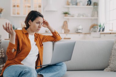 Laptop ekranına bakan, koltukta oturan kafası karışık bir kadının bilgisayar, virüs ya da kötü internet bağlantısı sorunu var. Sinirli kadın, film senaryosundan öfkelenmiş dizi veya film izliyor..