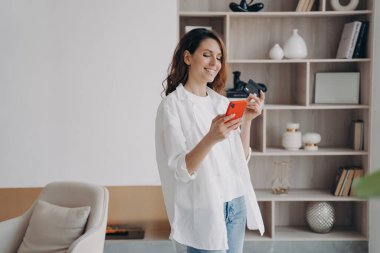 Gülümseyen kadın modern ev içinde banka kartı ve akıllı telefon tutuyor. Online alışveriş için banka hizmetini kullanan bir kadın güvenli bir şekilde evde nakit ödeme yapıyor. E-ticaret.