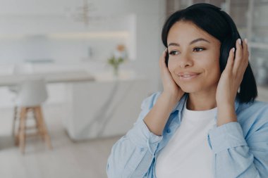 Genç melez romantik bayan kulaklıkla radyo dinliyor, hayal kuruyor ve gülümsüyor. Müzikten zevk alan mutlu Avrupalı kız. Evde hafta sonunun tadını çıkarıyorum. Duygular ve rahatlama.