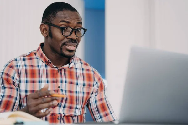Puzzled african american employee in glasses looking at laptop screen shocked by breakdown of computer or problems in work. Outraged black male is perplexed by program error or bad internet connection