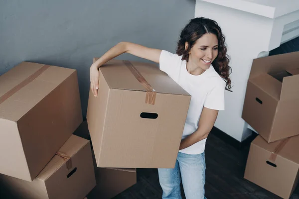 Excited spanish woman renting home. Boxes unpacking in new house. Lady is unloading cardboard boxes in room of apartment. Changes, improvement and new life concept.
