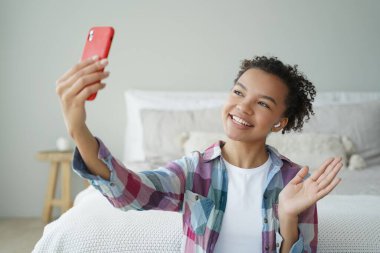 Videolu telefon görüşmesi. Kıvırcık Afrikalı Amerikalı kadın cep telefonuyla arkadaşıyla konuşuyor. Genç bayan kameranın önünde konuşuyor ve el sallıyor. Sanal iletişim konsepti. Genç kız yaşam tarzı..
