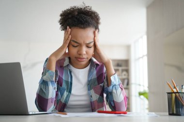 Aşırı çalışan afro öğrenci evde uzaktan kumanda okuyor ve başı ağrıyor. Genç liseli kız ödevden yorgun bir şekilde dizüstü bilgisayarın önünde oturuyor. Okulda uzaklık çalışmasında sorunlar.