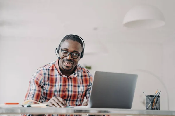 Afrykański Amerykanin Noszący Słuchawki Siedzący Przy Biurku Patrzący Ekran Laptopa — Zdjęcie stockowe