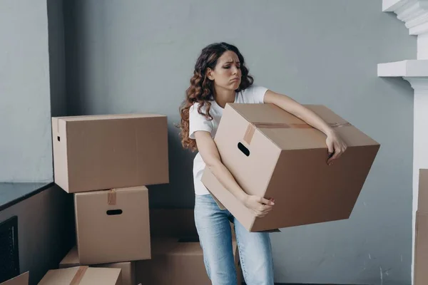 Tired young woman renter exhausted of carrying heavy cardboard boxes with things on moving day. Upset hispanic girl tenant frowning leaving rented apartment. Mortgage, real estate tenancy concept