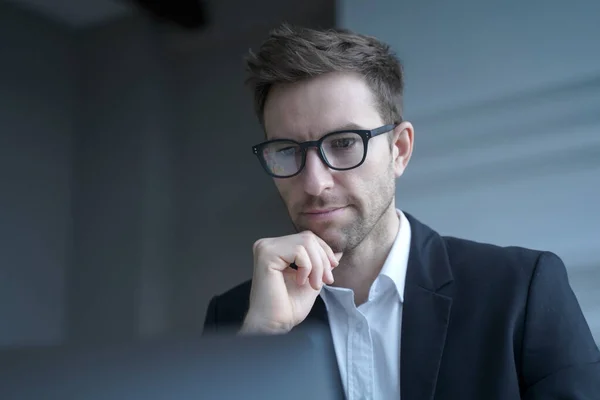 Focused German man family lawyer in formal wear thoughtfully looking at computer monitor while distantly working from modern home office carefully reading clients\' prenuptial agreement for signature