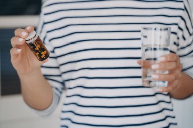 Avrupalı kadının elleri ilaç şişesi ve bir bardak su tutuyor. Tıpla terapi. Bayan takviye ve vitaminler alacak. Eczacılık ve tedavi. Ağrı kesici alıyorum..