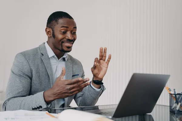 Pleased african american man manager showing ok gesture, talks with client by video call, working at laptop. Smiling satisfied black businessman shows okay sign to business partner, approves deal.