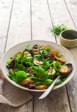 Fırında patates, ızgara kabak ve karışık salata sebze salatasını kırsal tabakta, doğal ahşap masada yakın planda bırakır.