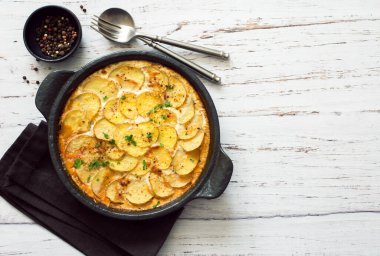 Fırında fırında patates peynirli ve kremalı güveç eski beyaz ahşap masadaki yemek tepsisinde servis ediliyor. Düz yatıyordu. Boşluğu kopyala