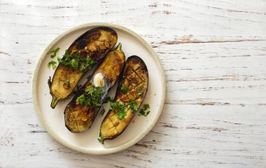Izgara patlıcan dilimleri ve beyaz ahşap arka planda beyaz tabakta otlar. Düz yatıyordu. Boşluğu kopyala