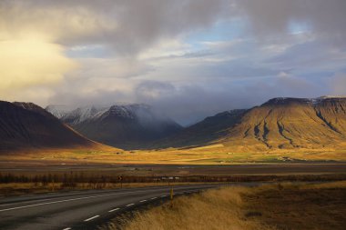 1. Yol ve İzlanda 'da güneş ve gölgelerle dolu bir dağ manzarası.