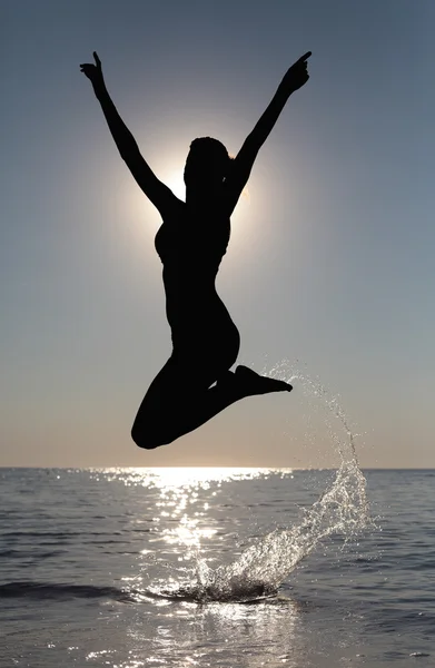 Silueta de chica joven, saltando contra de la puesta del sol del mar Imagen de archivo