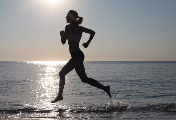 Schöne junge Sportlerin läuft am Strand. Stockbild