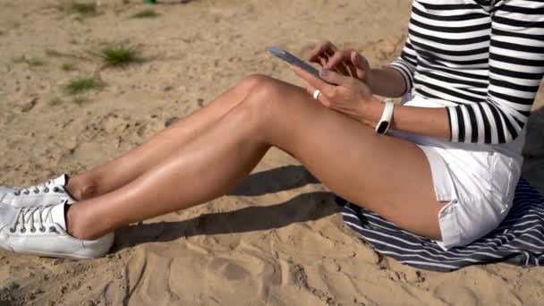 Millennial-Frau sitzt im Sand und hält Smartphone-E-Mails, positive junge Bloggerin Influencer teilen Inhalte während der Freizeit am Meer mit dem Handy — Stockvideo