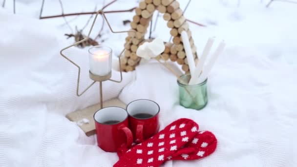 Vánoční ozdoby a dva šálky kávy na sněhu během Vánoc. Hořící svíčka a červené rukavice ve sněhu — Stock video
