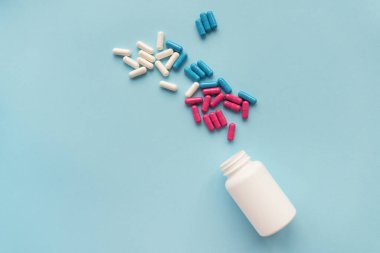 Mavi arka planda izole edilmiş açık plastik bir şişeden uçan çeşitli renkli haplar.