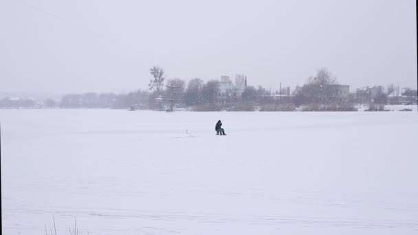 冬天和一个渔夫在冰上钓鱼，在下雪的过程中捕鱼。在湖心区天气不好的时候钓到栖鱼 — 图库视频影像