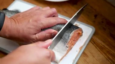 Plastik tahtada insan kesimi kırmızı balık. Şef mutfakta somon kesiyor. Aşçı alabalığı biftekle keser. Elleri kesilmiş ahbap. Keskin çelik bir bıçakla tahtadan taze balıkları ince ince dilimlere ayırmak.