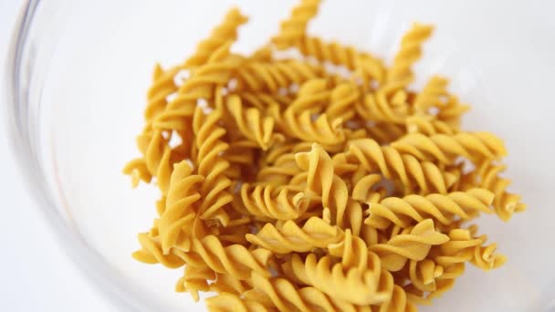 Celozrnné tmavě žluté nevařené těstoviny fusilli. Italské makarony padající na hromadu v průhledném talíři zblízka. Koncept středomořské kuchyně — Stock video