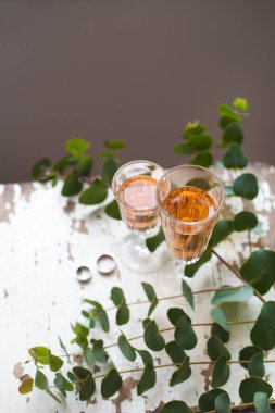 Okaliptüs dalları eski bir masanın üzerinde bir bardak gül şarabı ve alyansla