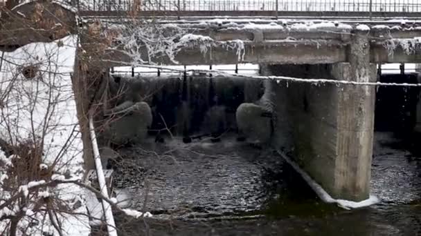 L'acqua cade da una diga di cemento in pieno inverno e cade neve. La gente cammina sulla diga e le auto stanno guidando — Video Stock