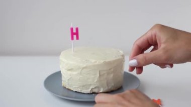 Cooking and decoration of cake candles in the form of letters. Girl hand pastry chef in the kitchen decorating white cream cake word - happy. Young woman in kitchen makes beautiful birthday cake.