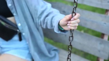 Young girl swinging on swing in park holding on to chain. Wooden swing with swinging free, happy woman outdoors. Swing and dreams of flying. Travel in spring summer in nature. Healthy lifestyle.