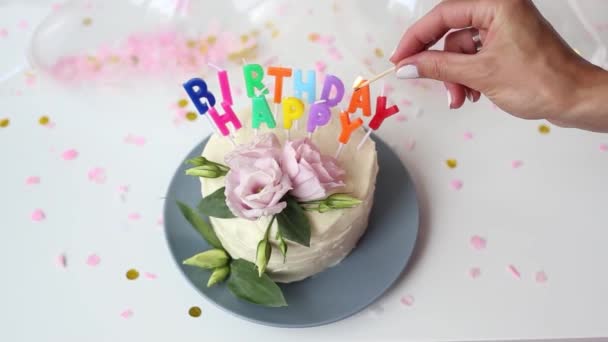 Молодая женщина, зажигая свечи торта в виде слова - с днем рождения, и тушит матч. Закрыть кадры праздничного пирога с белым кремом. Торт на день рождения с пылающими красочными свечами. — стоковое видео