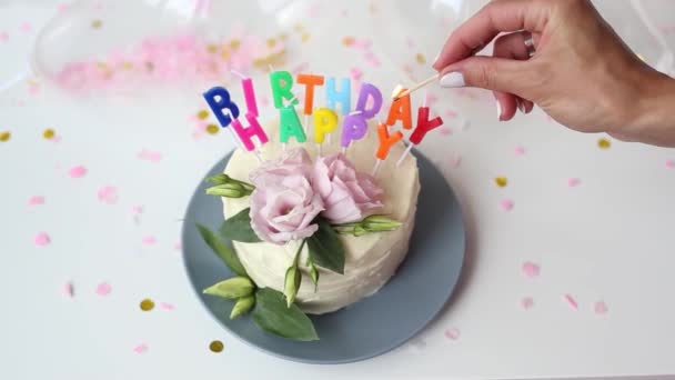 Jovem Iluminando as Velas de um Bolo na forma de uma palavra - Feliz Aniversário, e apaga o jogo. Feche a filmagem da torta festiva de creme branco. Bolo de aniversário com velas coloridas ardentes. — Vídeo de Stock