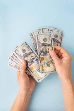 Mavi arka planda izole edilmiş 100 dolarlık banknotları sayan kadın eller.