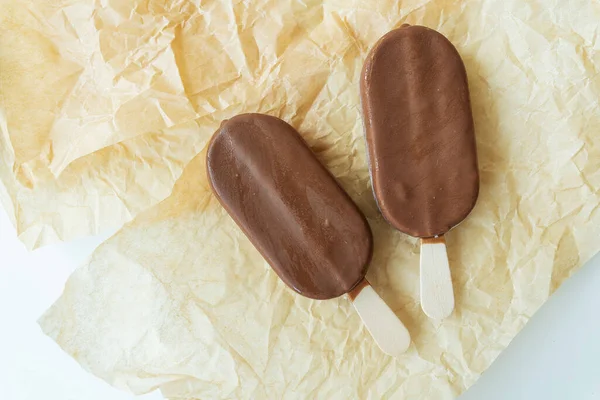 Chocolate ice cream on a stick lies on parchment covered with chocolate, warm, cold, delicious ice cream. Summer rest. View from above