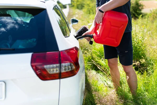 The driver refuels the empty tank of the car from a red canister on the side of the road. Fuel problem, force majeure