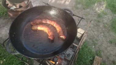 Barbekü ızgarasında ev yapımı lezzetli sosis. İki sosis kızartma tavasında kızgın yağda kızarır.