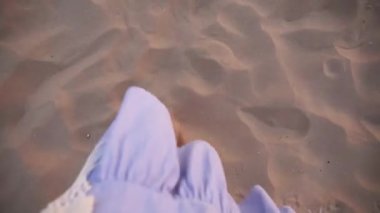 Close up of female feet walking on golden sand at the beach. Slender legs of young woman stepping at sand - top view. Barefoot girl at the sea shore. Summer vacation holiday - walk along the beach