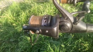 Unwinding fishing line or cord from a reel spool for rod pod against the background of green grass. Fish biting on a sunny summer day. Catching carp and pike on a spinning reel with a baitrunner