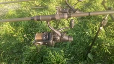 Unwinding fishing line or cord from a reel spool for rod pod against the background of green grass. Fish biting on a sunny summer day. Catching carp and pike on a spinning reel with a baitrunner